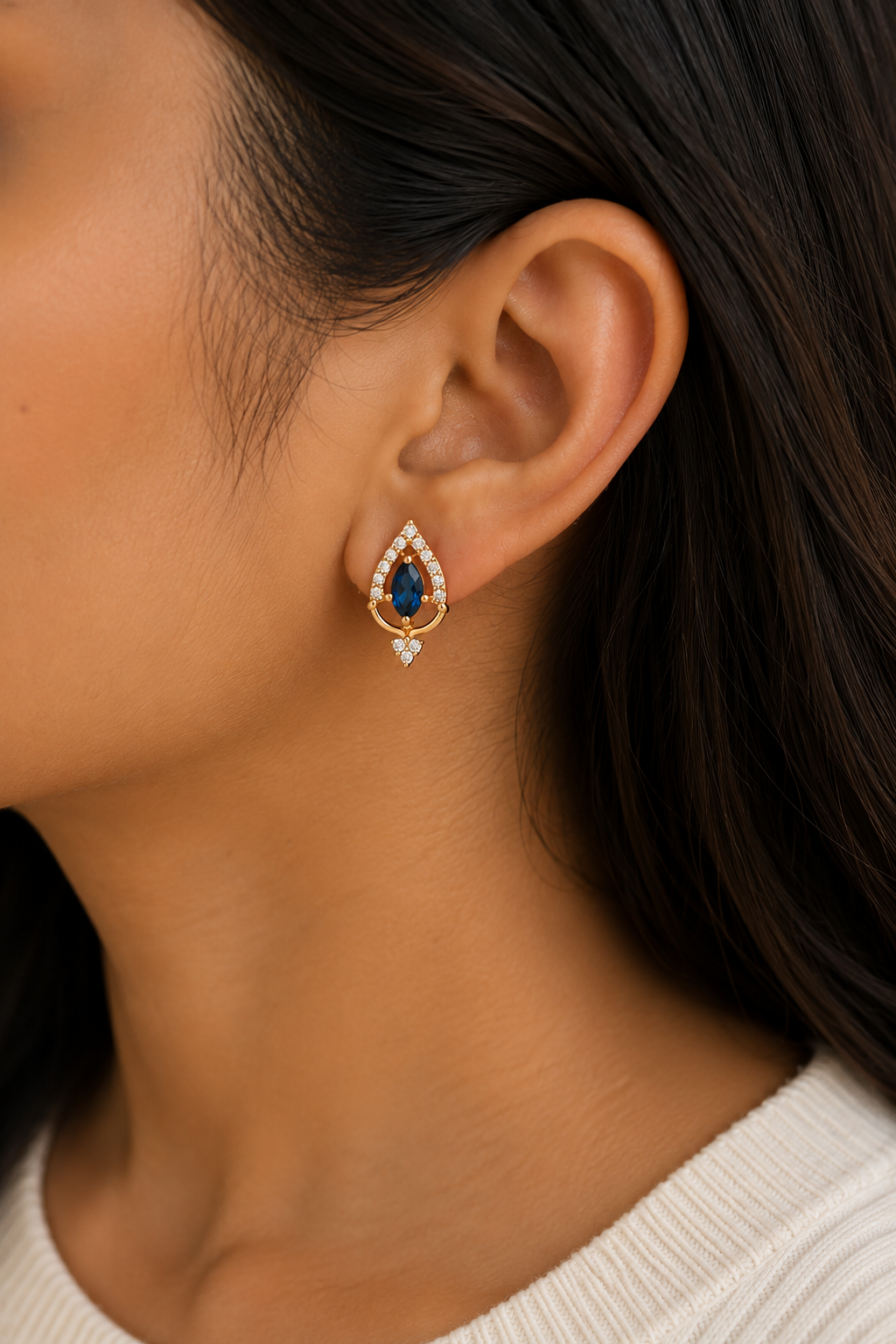 Teardrop Sapphire Gold Earrings worn on the ear, blue stone halo studs with a small drop